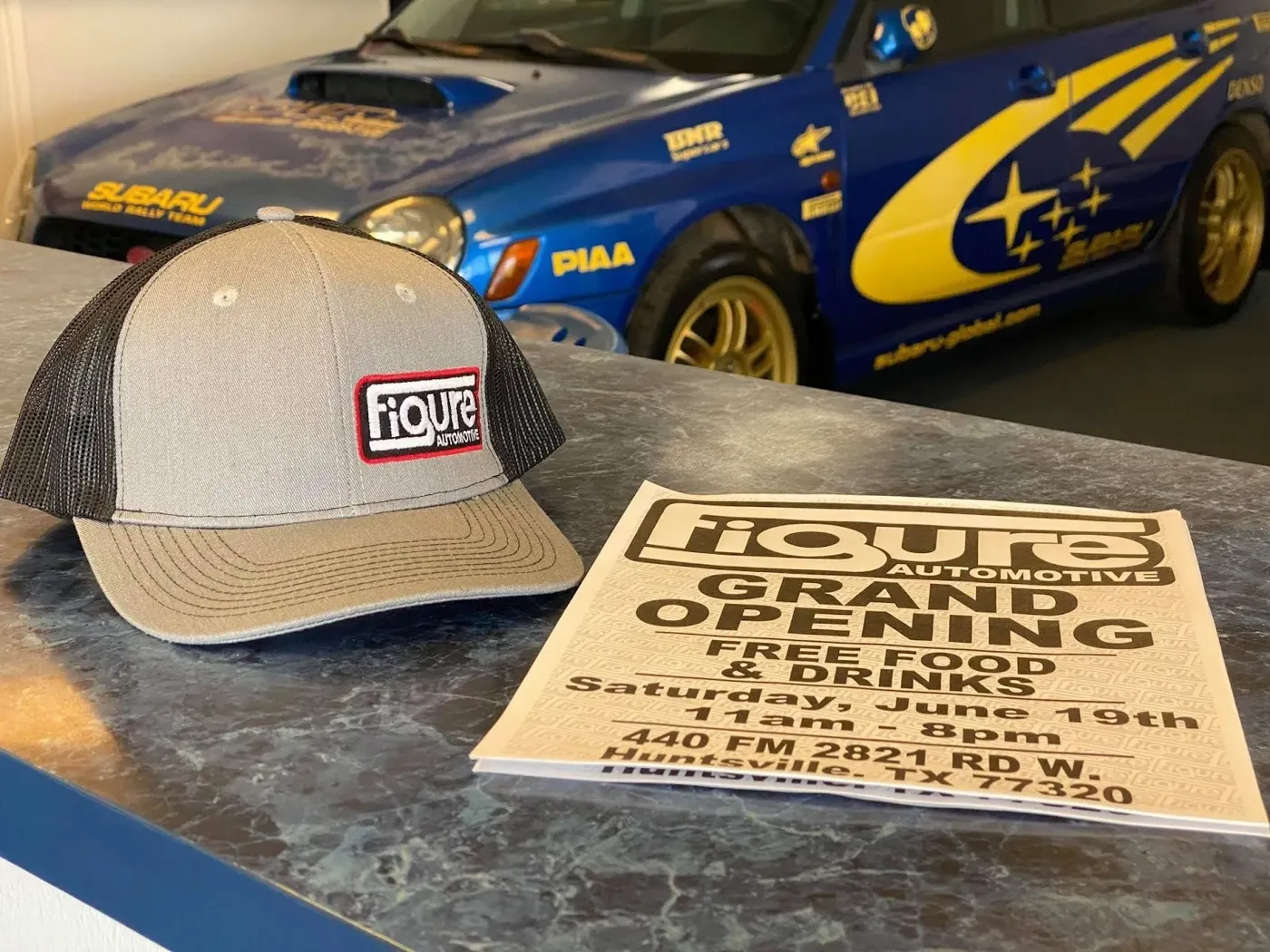 A Figure Automotive cap next to the shop's grand opening flyer