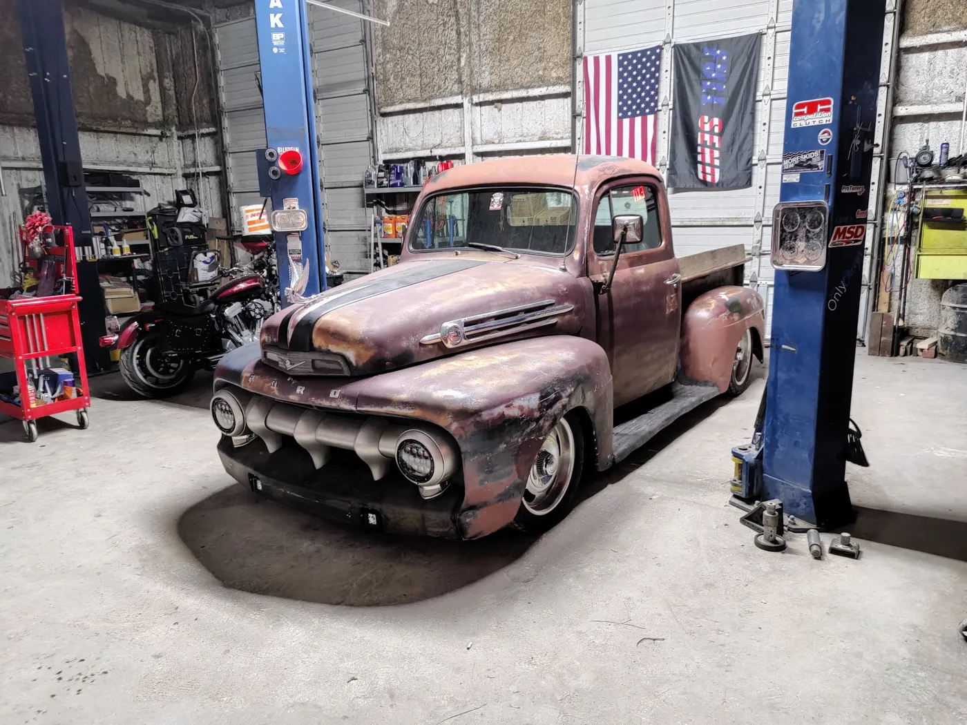 Patina classic Ford F-1 pickup parked between lifts under American flags