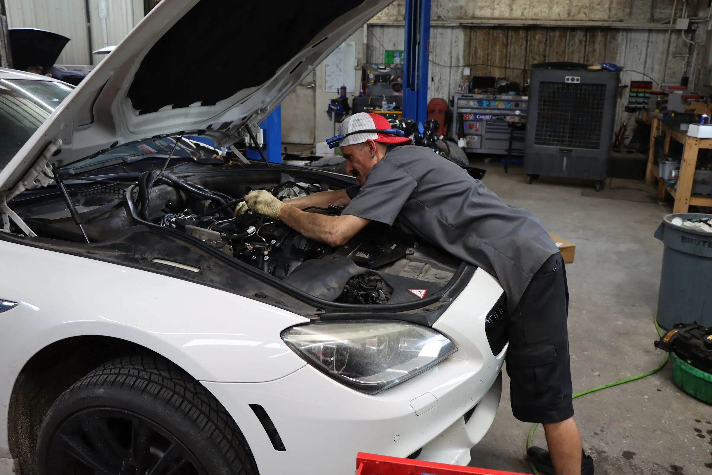 Figure Automotive technician working under the hood of a white BMW in the shop
