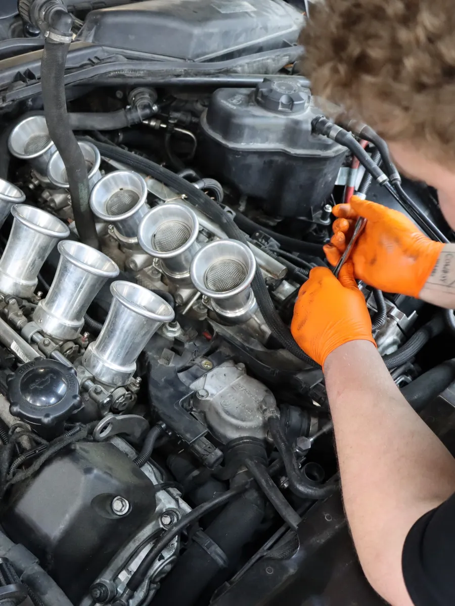 Gloved hands working on a V8 fitted with individual throttle bodies