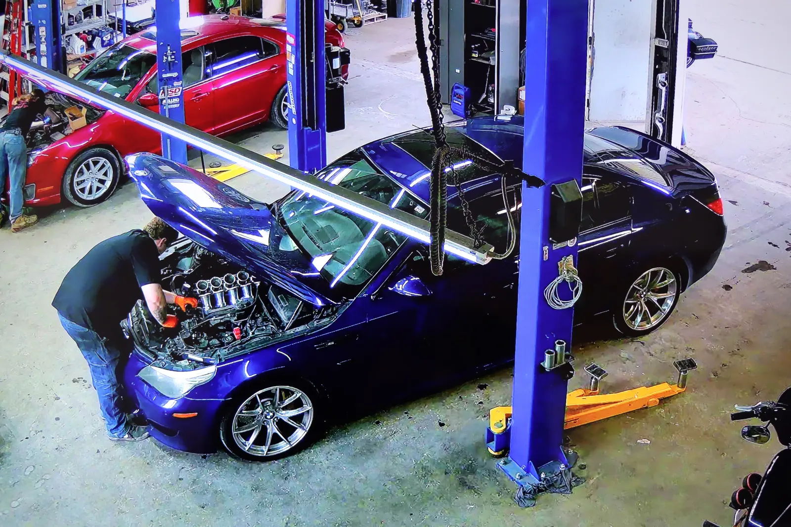 Technician under the hood of a blue BMW M5 between the blue lifts