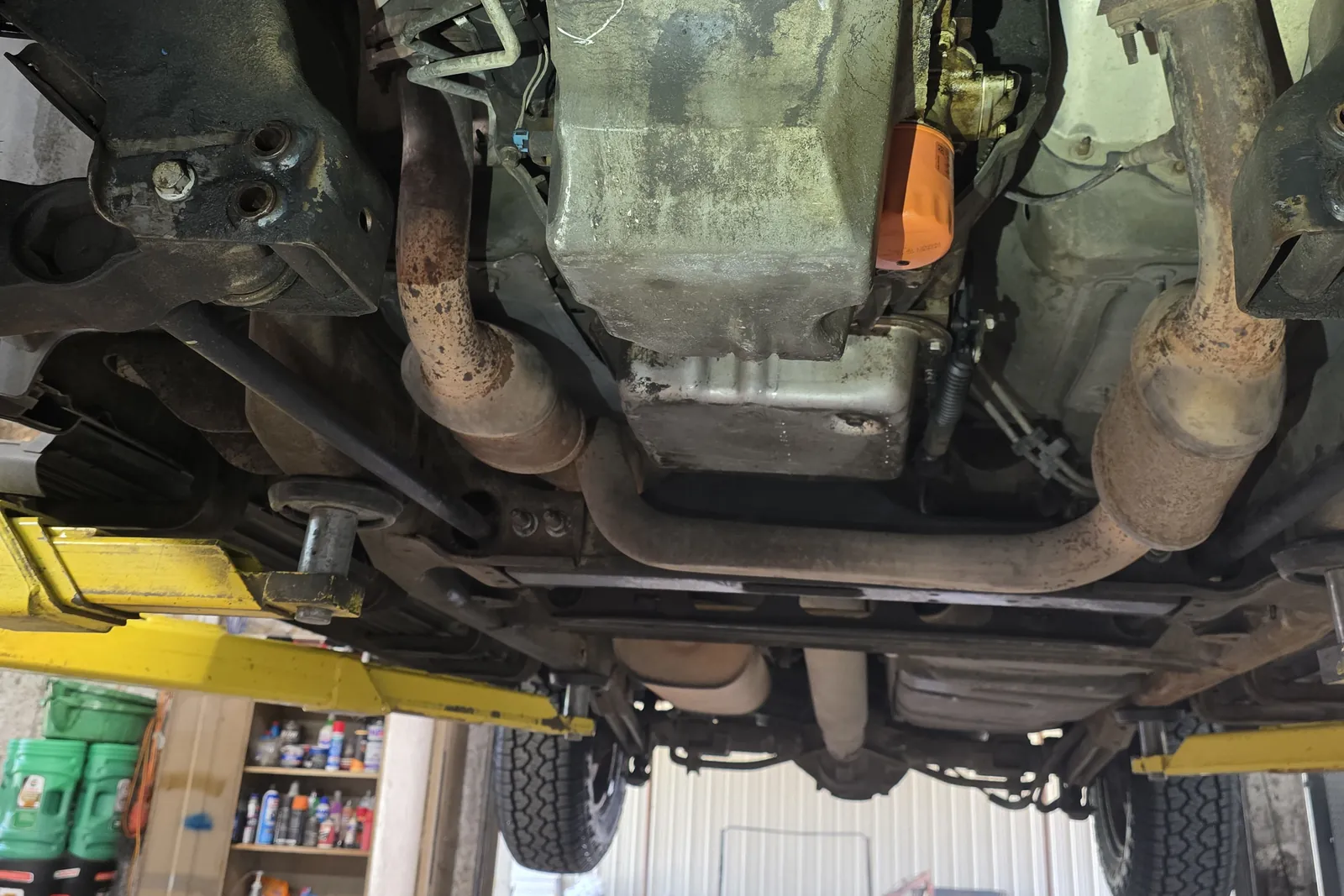 Underside of a vehicle on a lift showing the oil pan and a fresh orange oil filter