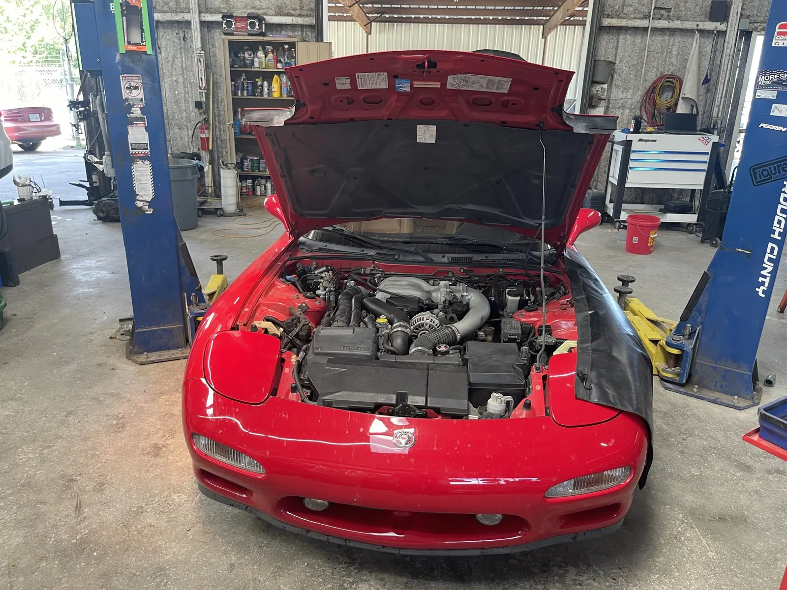 Red Mazda RX-7 with the hood up between the lifts
