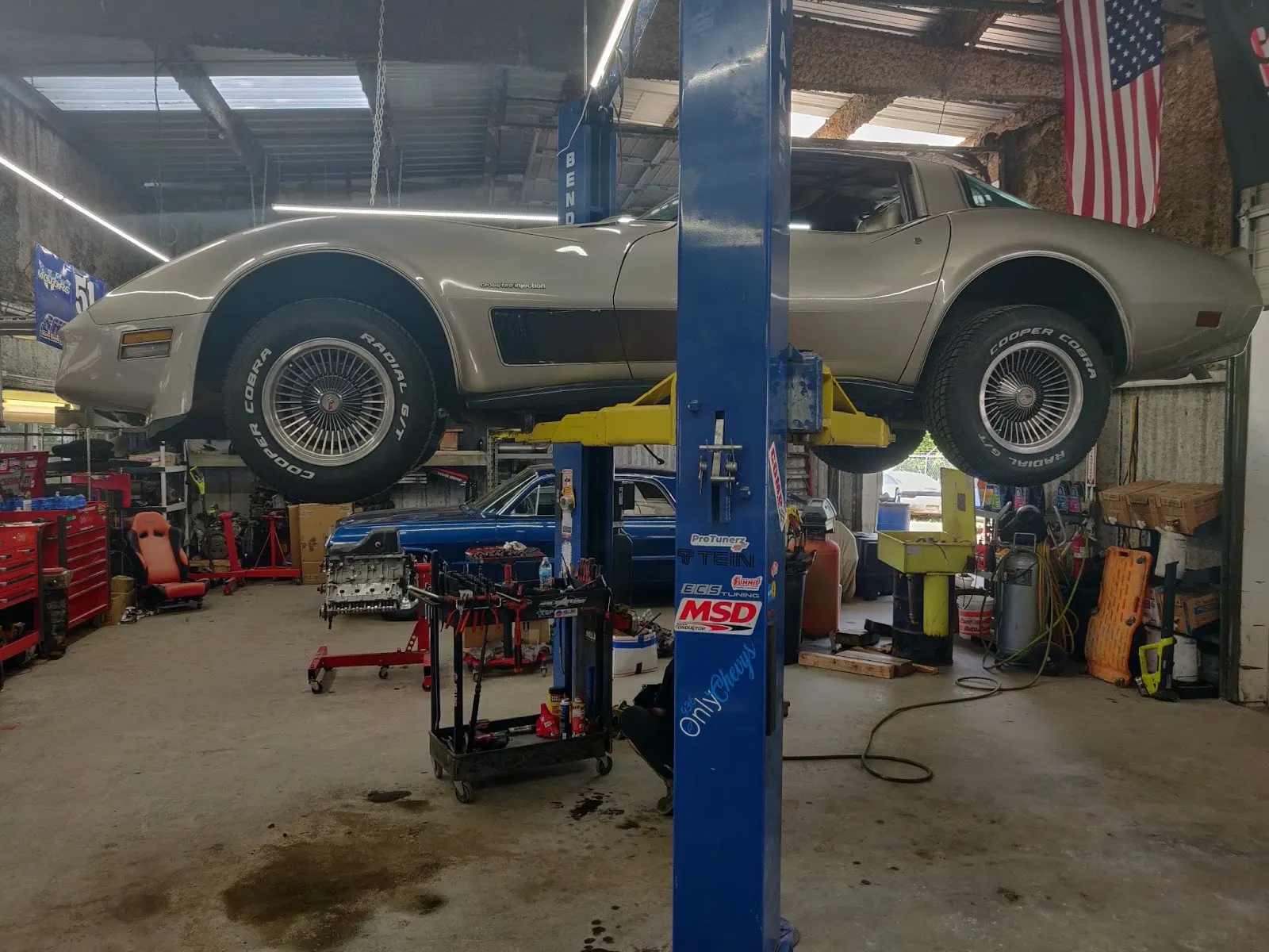 Silver C3 Chevrolet Corvette raised on a lift under an American flag